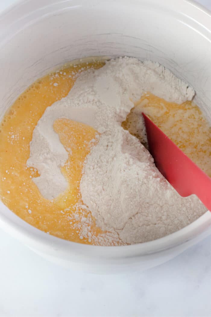 adding butter and eggs to the cake mix in a white mixing bowl.