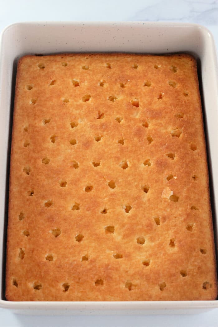 poking holes in a baked white cake.