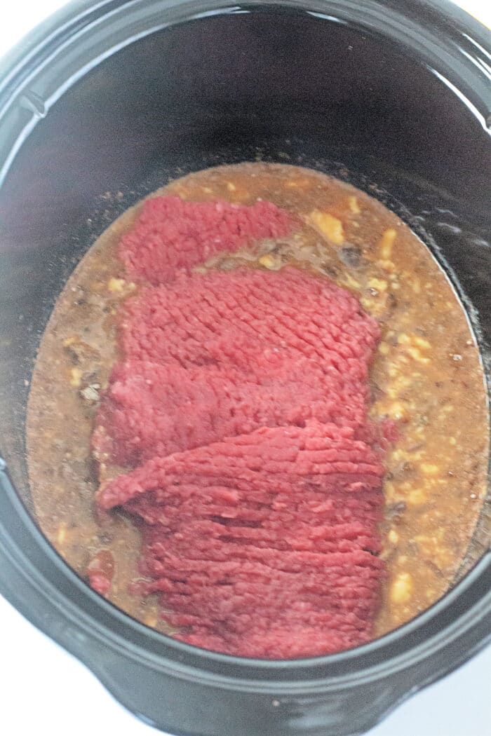 adding the cube steaks to the slow cooker.