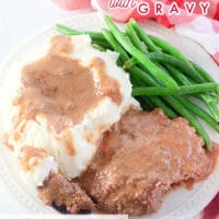Crockpot cube steak on a plate next to mashed potatoes and green beans, topped with gravy.