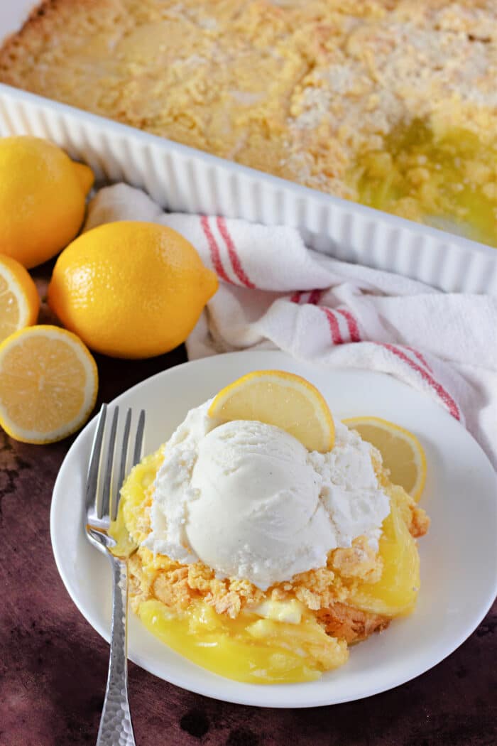 Lemon Dump Cake on a white plate with fresh lemons.