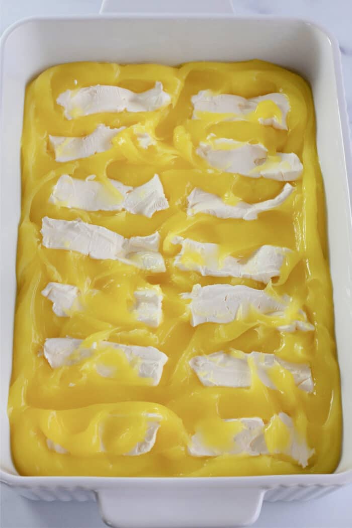 slices of cream cheese over top of lemon pie filling in a baking dish.