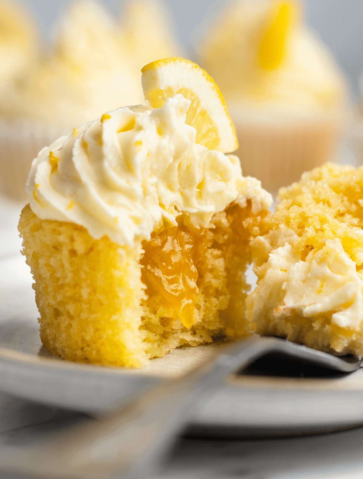 A lemon cupcake on a plate with a bite on a fork