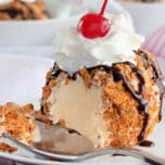 Fried Ice Cream topped with whipped cream and a cherry, with a spoonful missing.