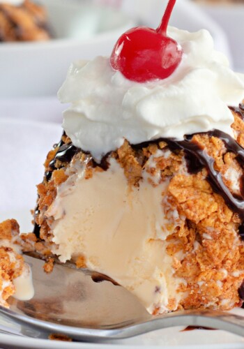Fried Ice Cream topped with whipped cream and a cherry, with a spoonful missing.