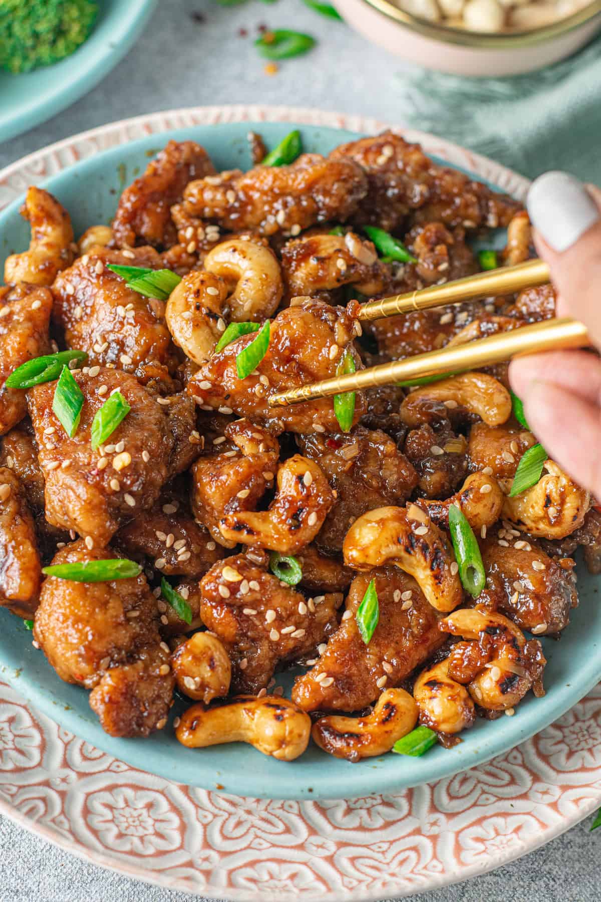Chopsticks holding a piece of cashew chicken over a plate