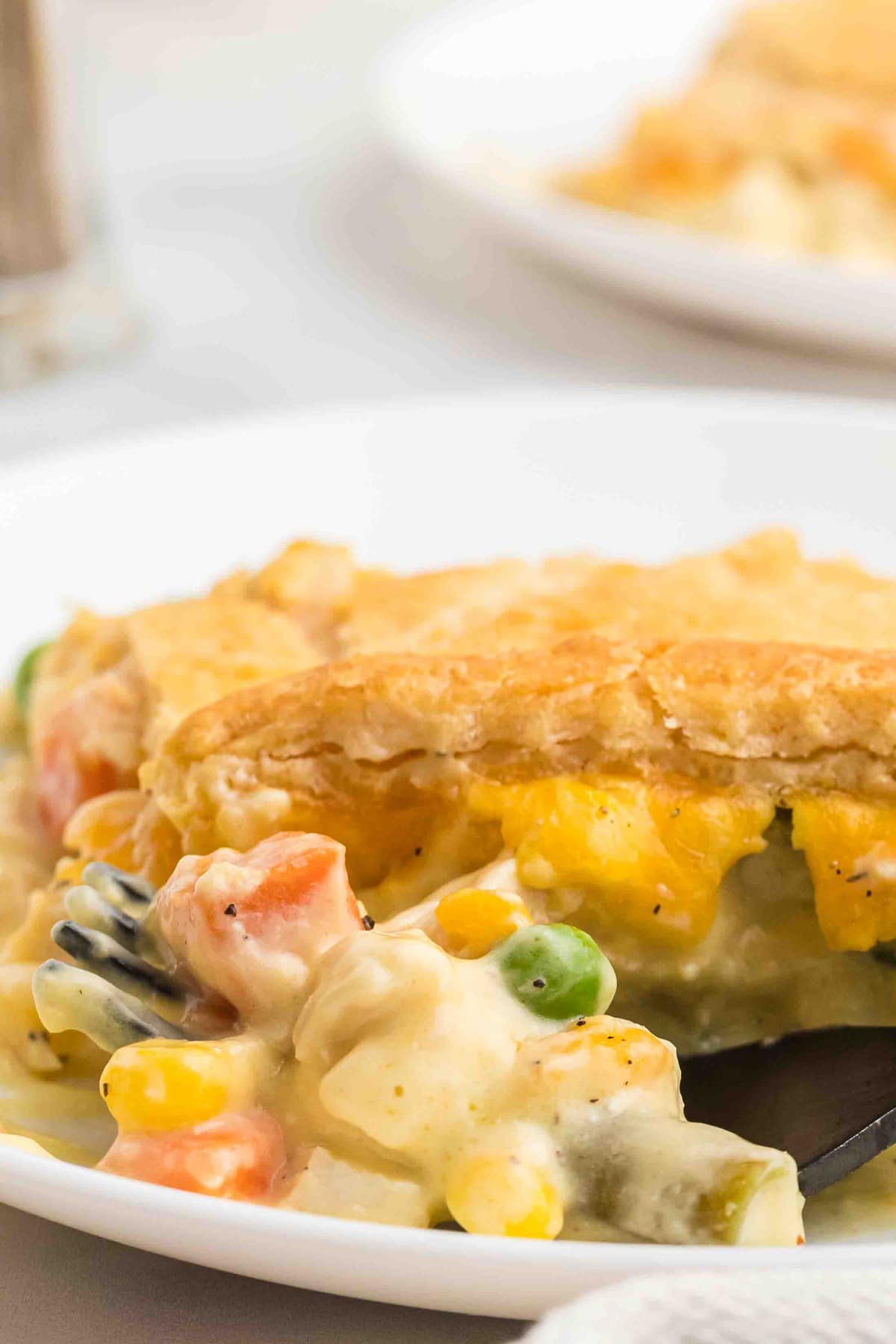 A spoonful of chicken pot pie casserole in front of a slice on a plate