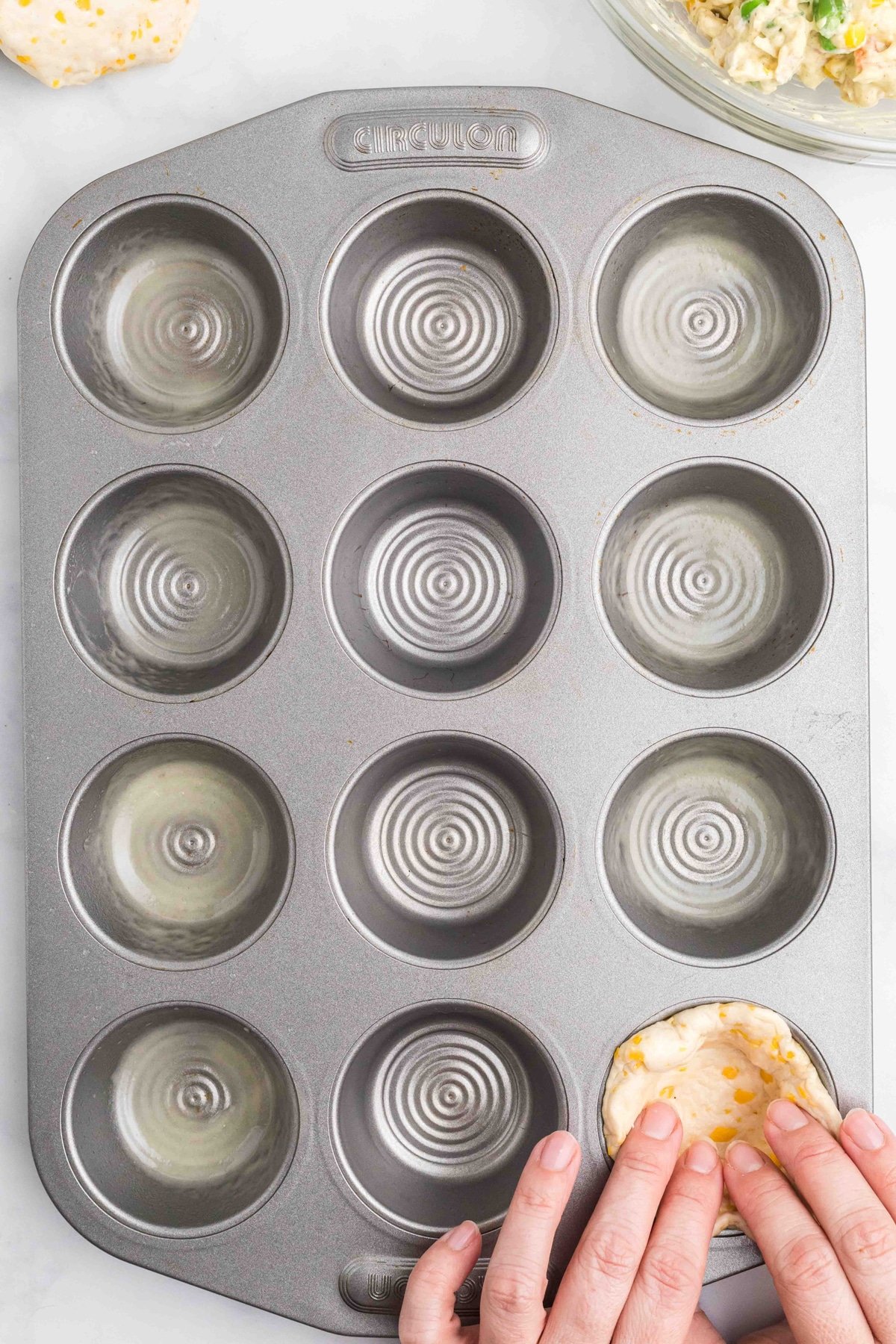 A hand pressing a biscuit into a muffin tin
