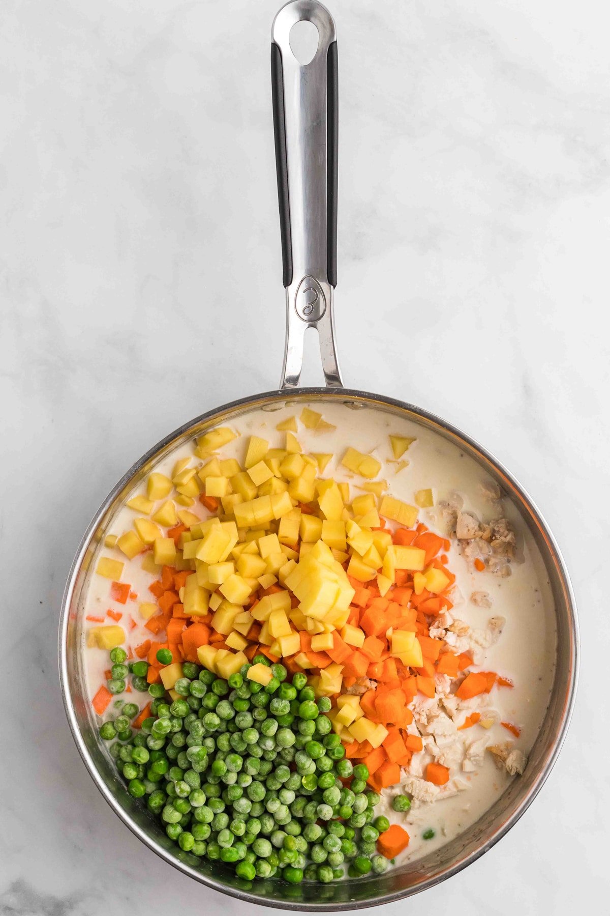 Peas, carrots, and potatoes added to pot pie filling in a pan