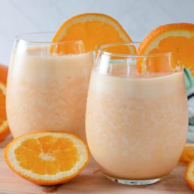 Two Orange Julius drinks in glasses garnished with whipped cream and orange slices.