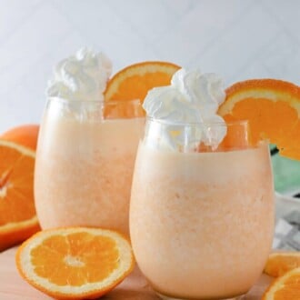 Two Orange Julius drinks in glasses garnished with whipped cream and orange slices.