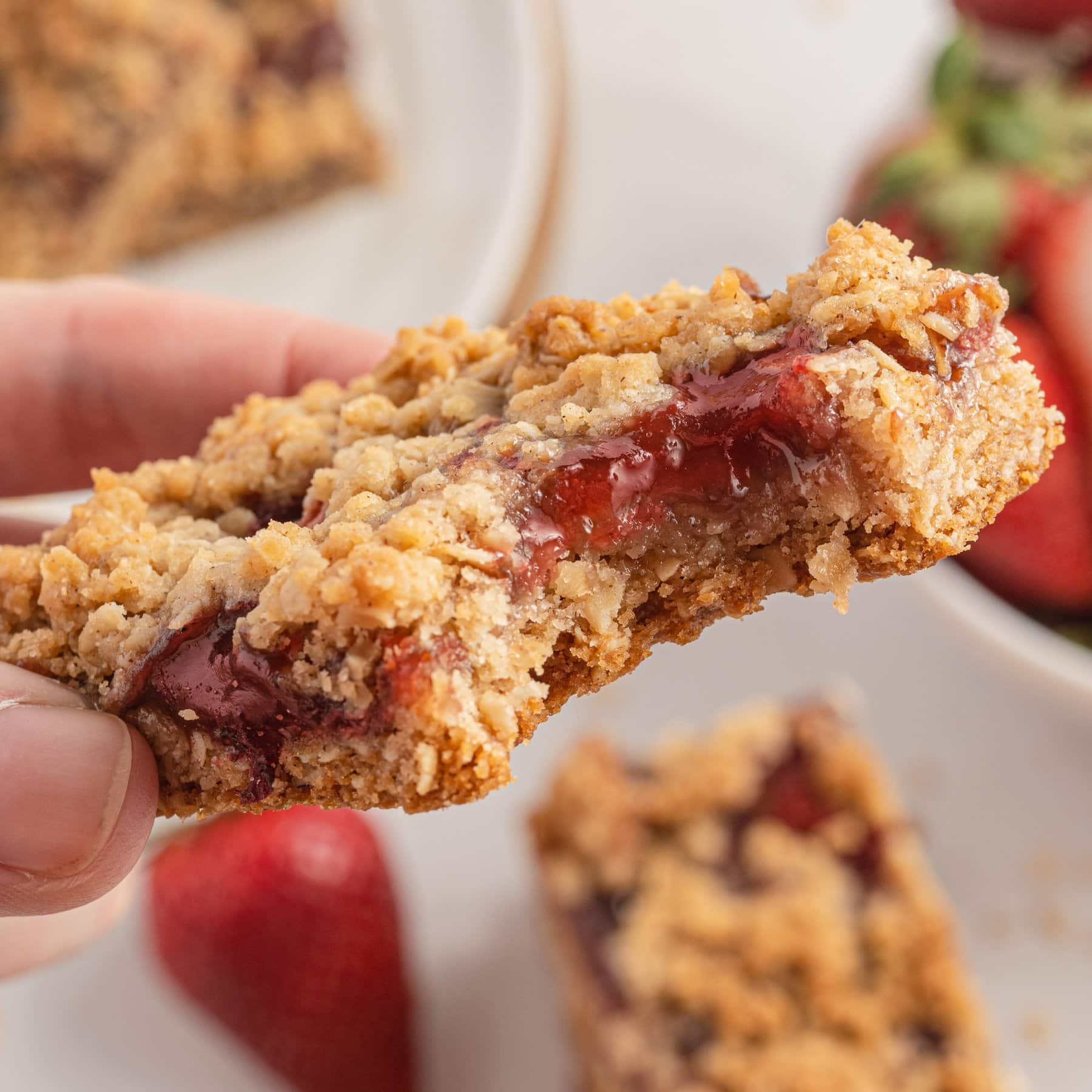A hand holding a strawberry oatmeal bar with a bite missing.
