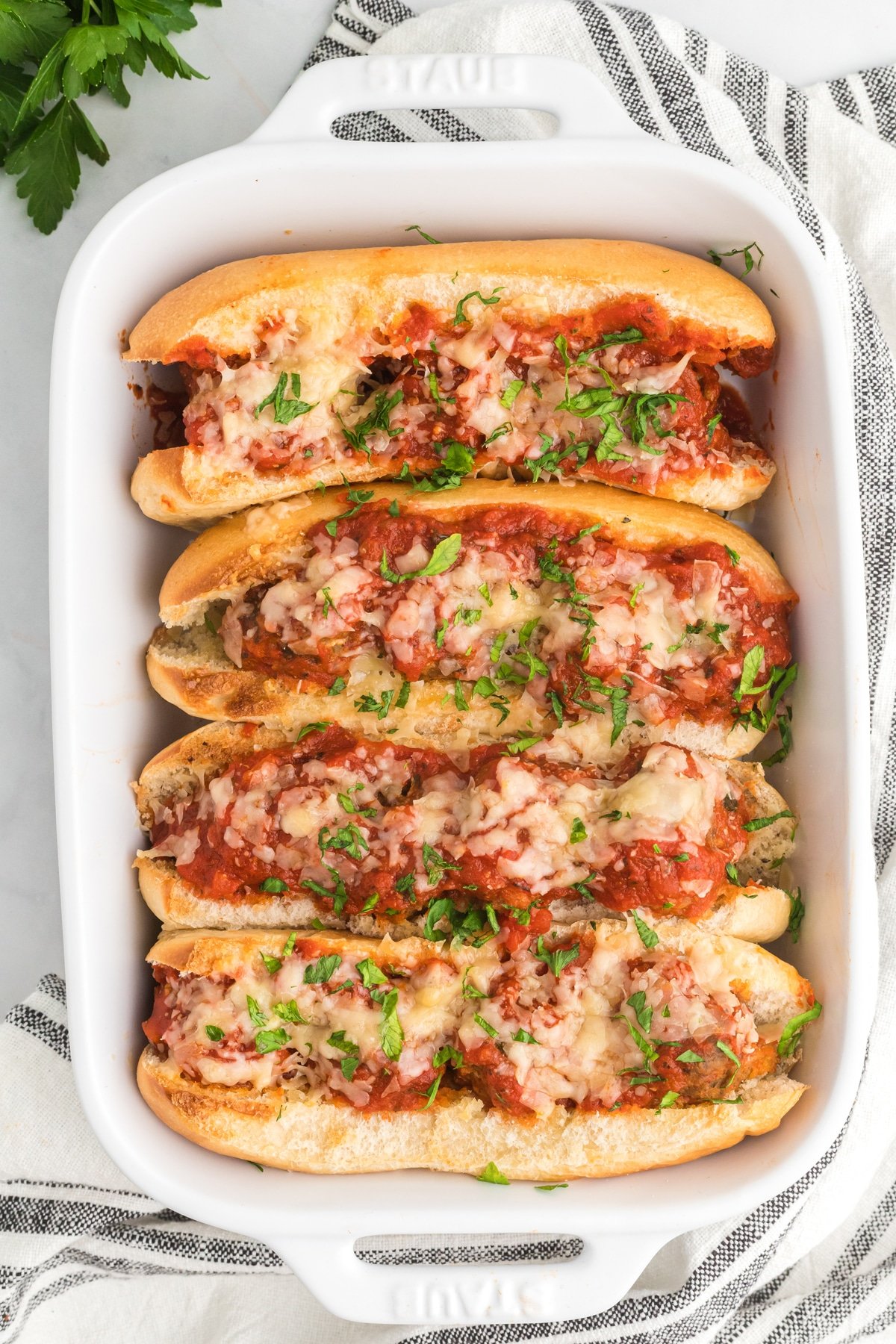 Meatball subs in a baking dish topped with cheese and parsley