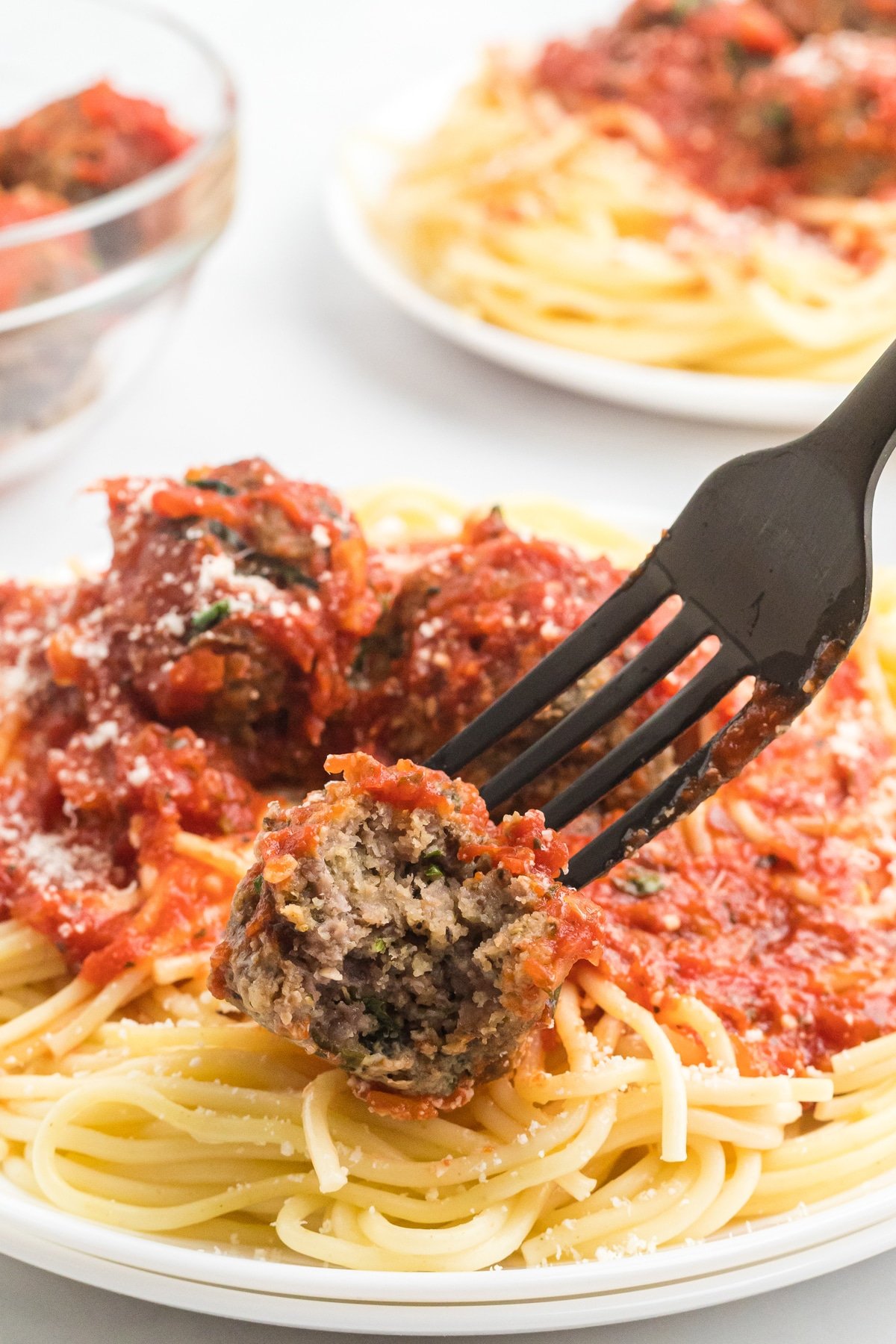 A meatball on a fork over a plate of spaghetti