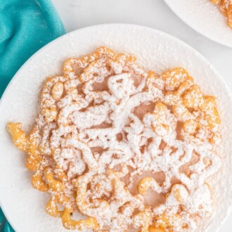 Top view of a funnel cake topped with powdered sugar on a plate.