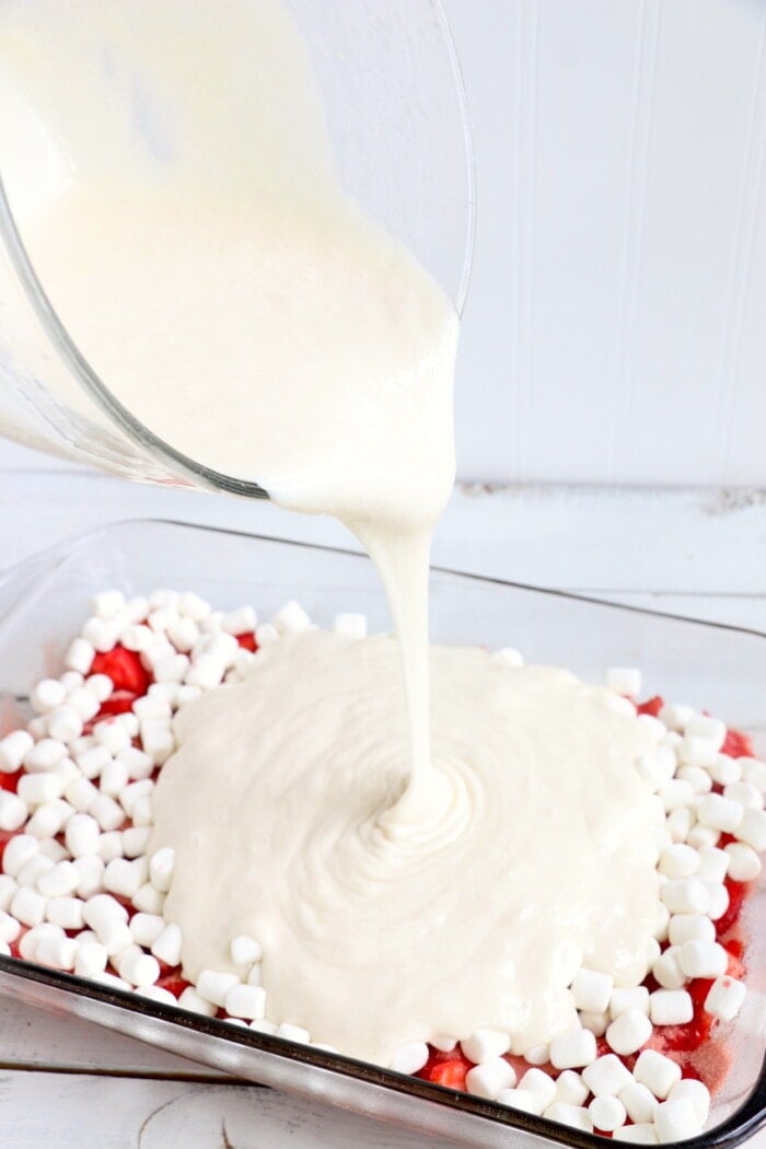 pouring cake batter over marshmallows and strawberries