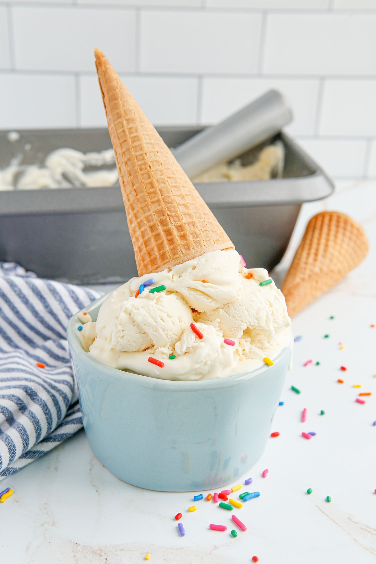 A bowl of vanilla ice cream topped with sprinkles and an ice cream cone