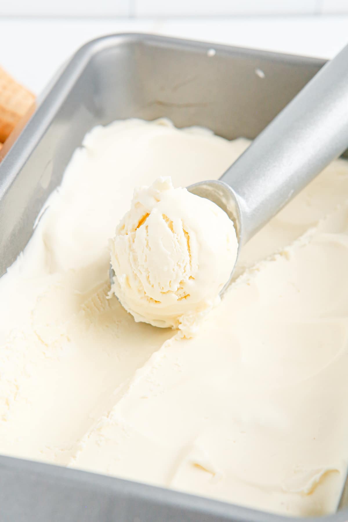 An ice cream scoop scooping vanilla ice cream from a loaf pan