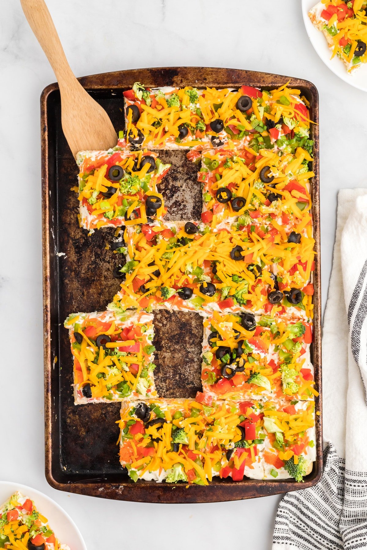 Crescent roll veggie pizza on a baking sheet with squares missing