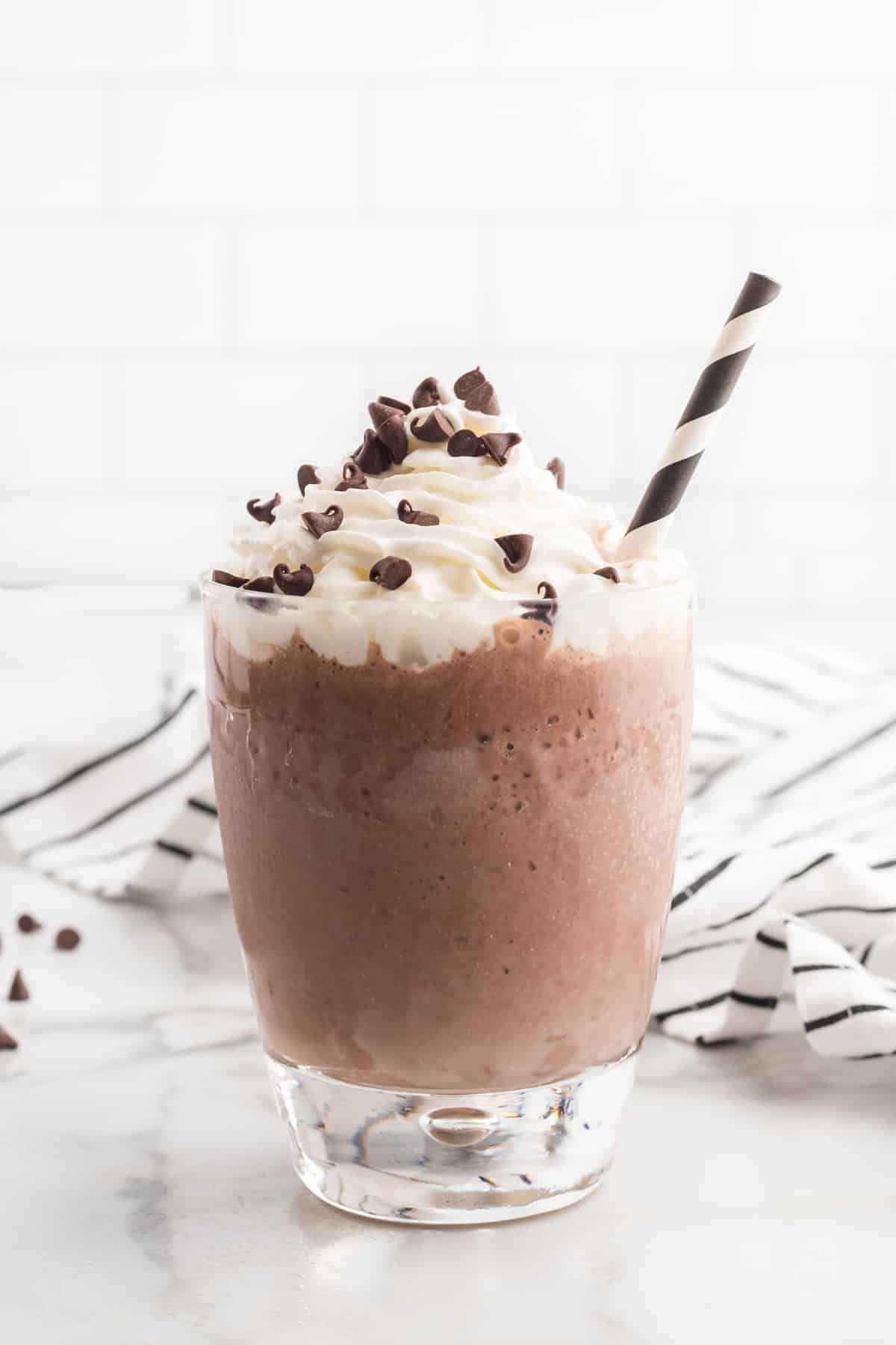 A frozen hot chocolate in a glass topped with whipped cream and chocolate chips