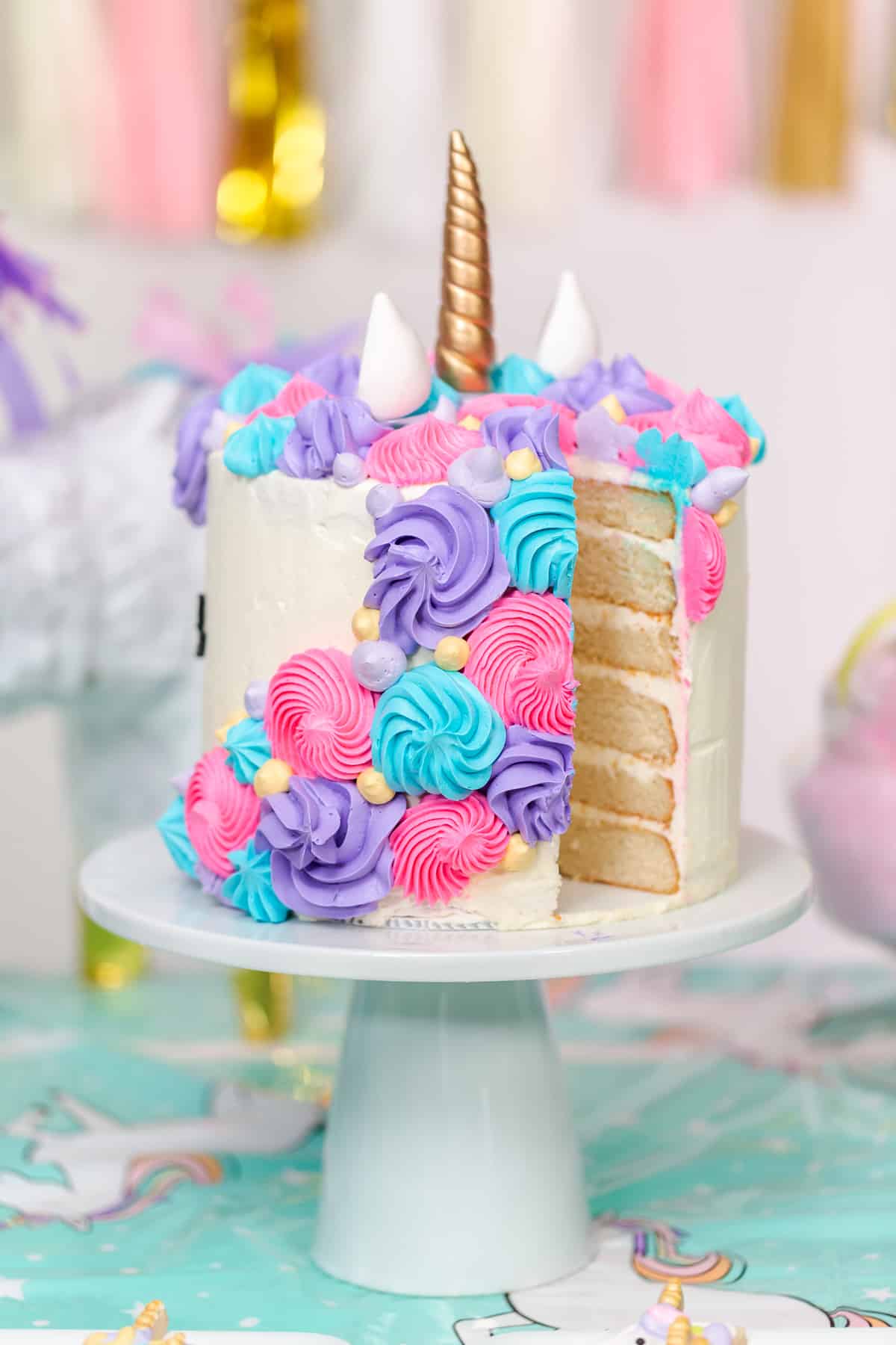 A unicorn layer cake on a cake stand, with a slice missing