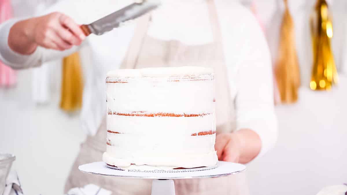 A hand turning a layer cake and spreading the frosting