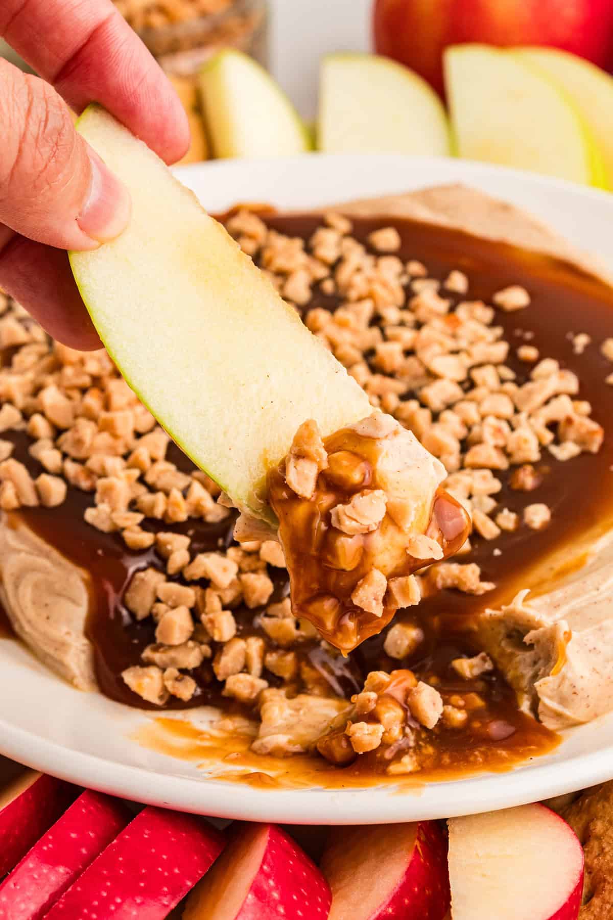 Ready in 5 minutes, this Caramel Apple Dip is made with cream cheese, brown sugar, and caramel sauce for an easy fall treat. A hand dipping an apple slice in cream cheese caramel apple dip