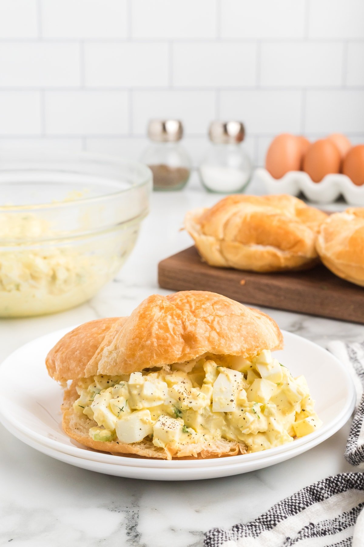 An egg salad croissant sandwich on a white plate