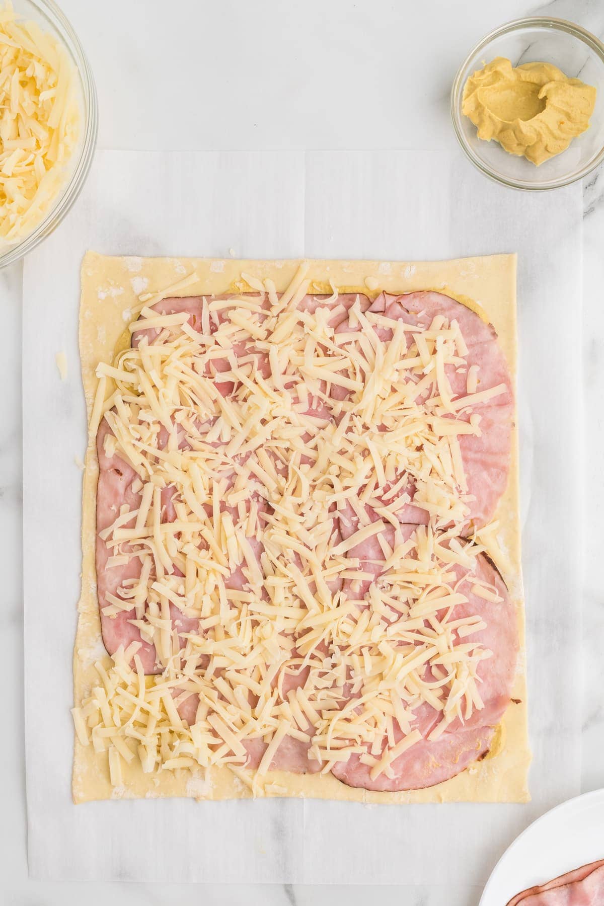 Grated cheese and slices of ham on a puff pastry