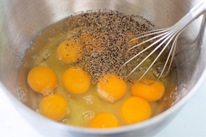 whisking eggs and seasonings in a metal bowl.