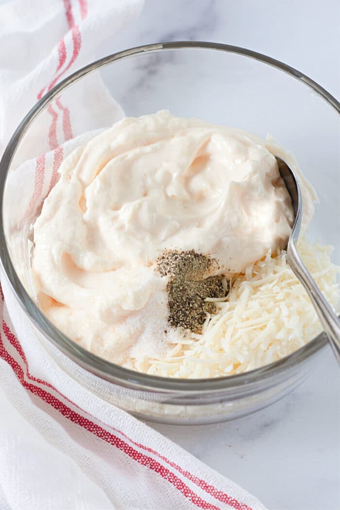 mixing together mayonnaise, seasonings, and parmesan cheese in a clear bowl.