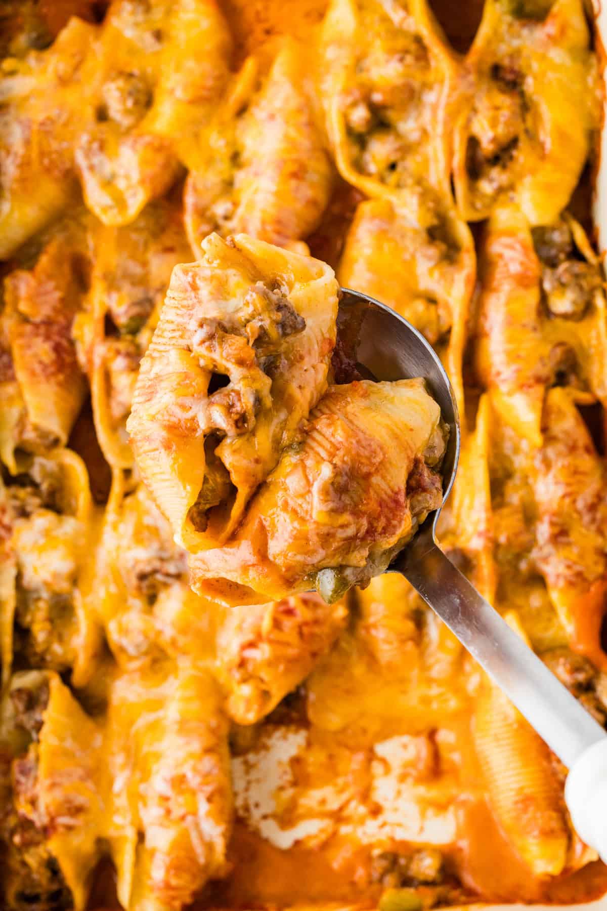Jumbo shells are stuffed with seasoned ground beef and topped with queso, taco sauce, and shredded cheese to make these Taco Stuffed Shells. Overhead view of taco stuffed shells on a spoon