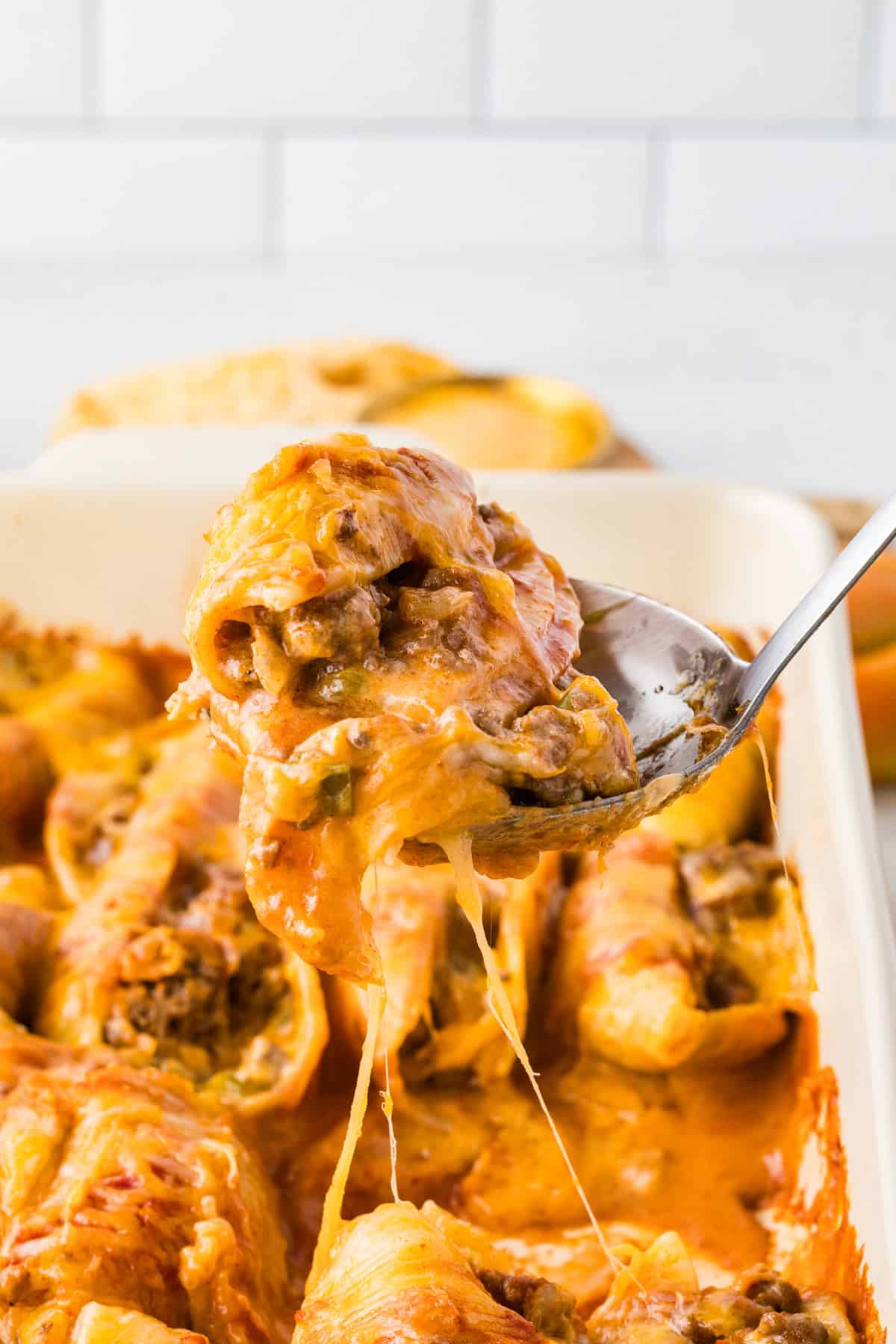 Close up of taco stuffed shells on a spoon over the baking dish