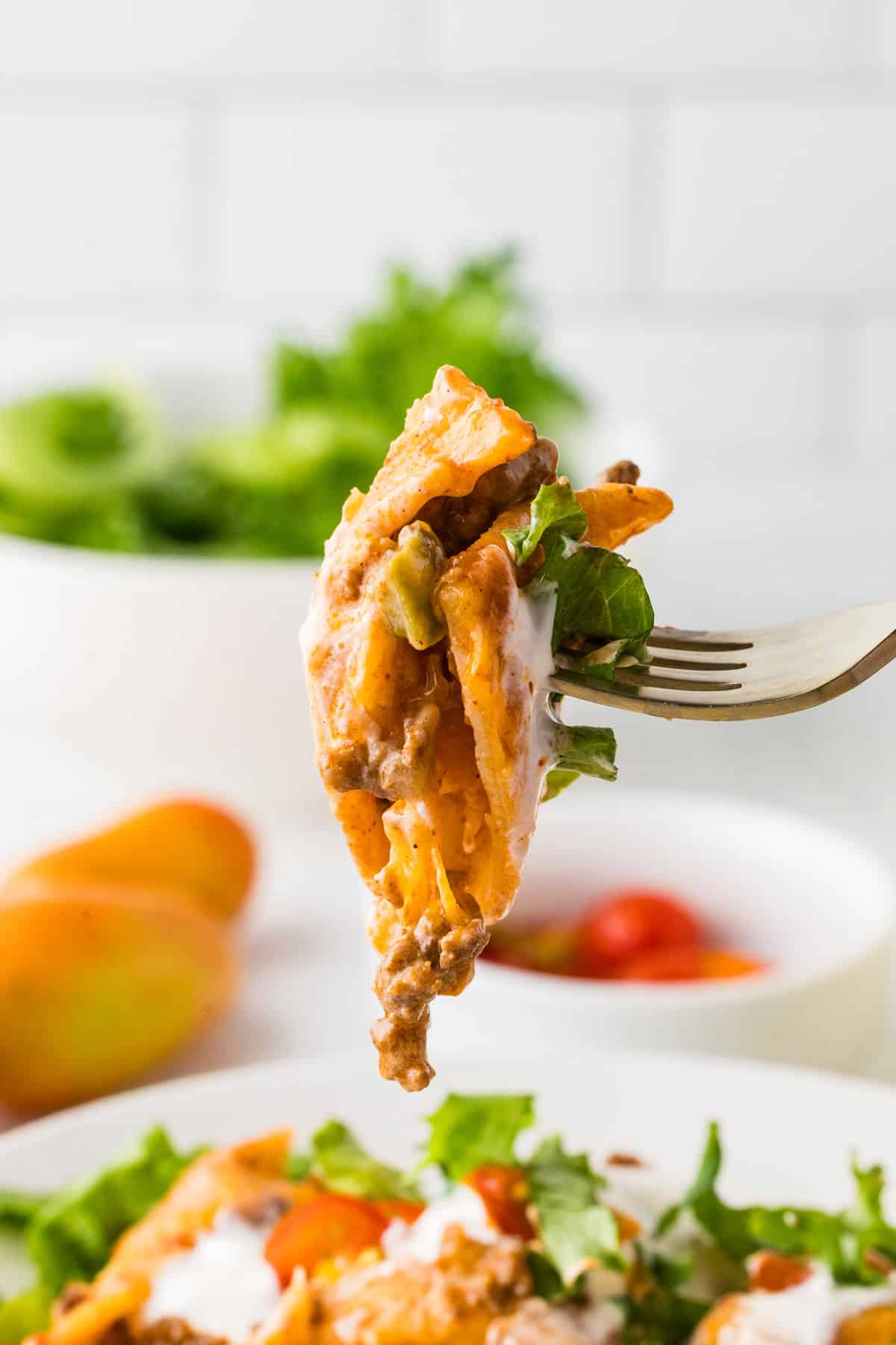 Jumbo shells are stuffed with seasoned ground beef and topped with queso, taco sauce, and shredded cheese to make these Taco Stuffed Shells. A bite of taco stuffed shells on a fork