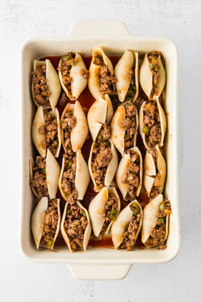 Jumbo shells are stuffed with seasoned ground beef and topped with queso, taco sauce, and shredded cheese to make these Taco Stuffed Shells. Jumbo pasta shells stuffed with meat in a casserole dish