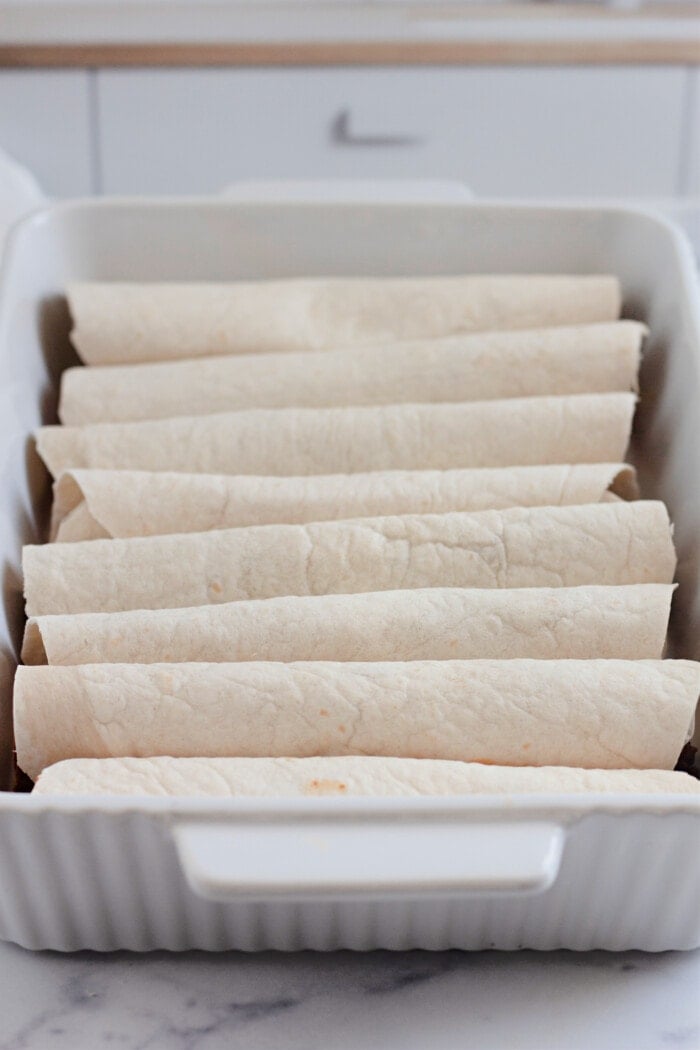 a casserole dish filled with rolled and filled tortillas.