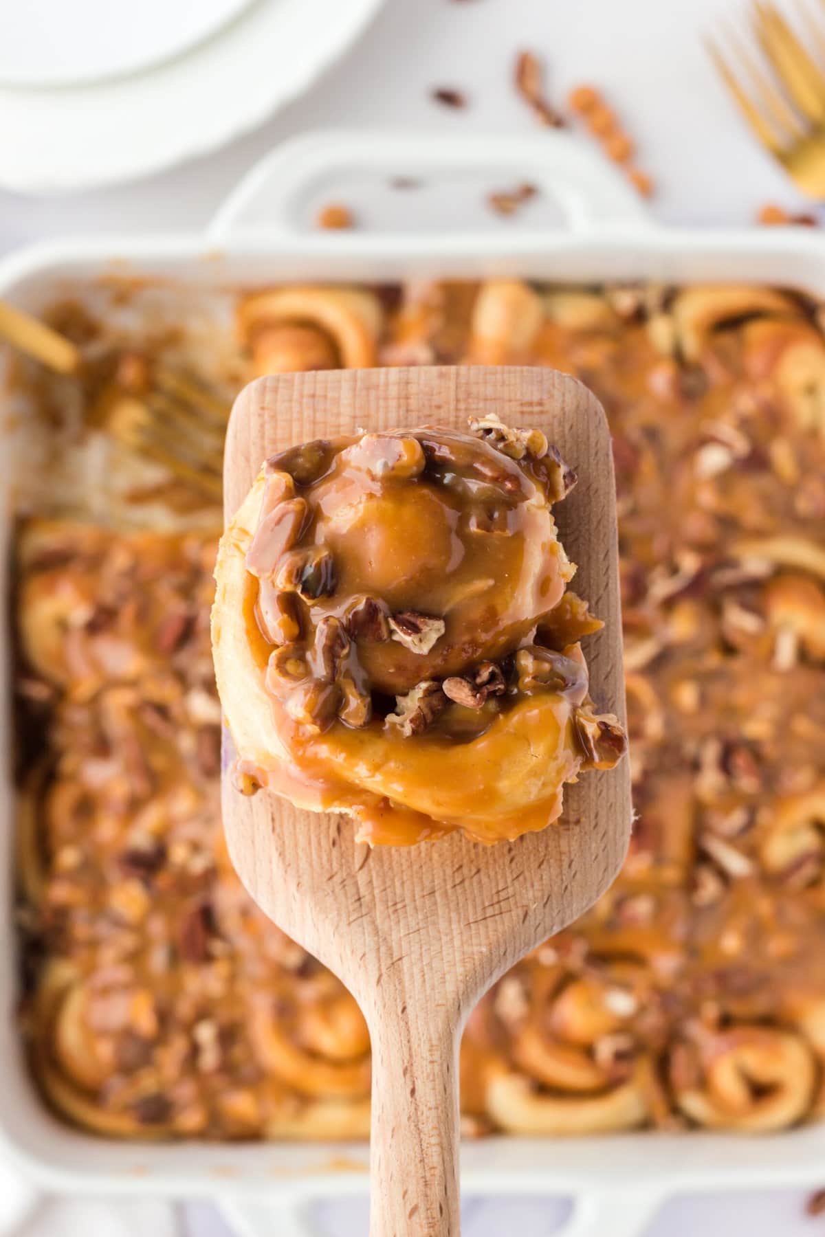 A wooden spatula lifting up the Caramel Pecan Cinnamon Roll.