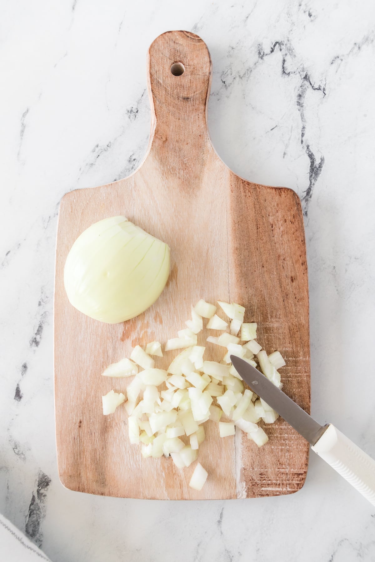 A whole onion on a cutting board next to a pile of diced onion.