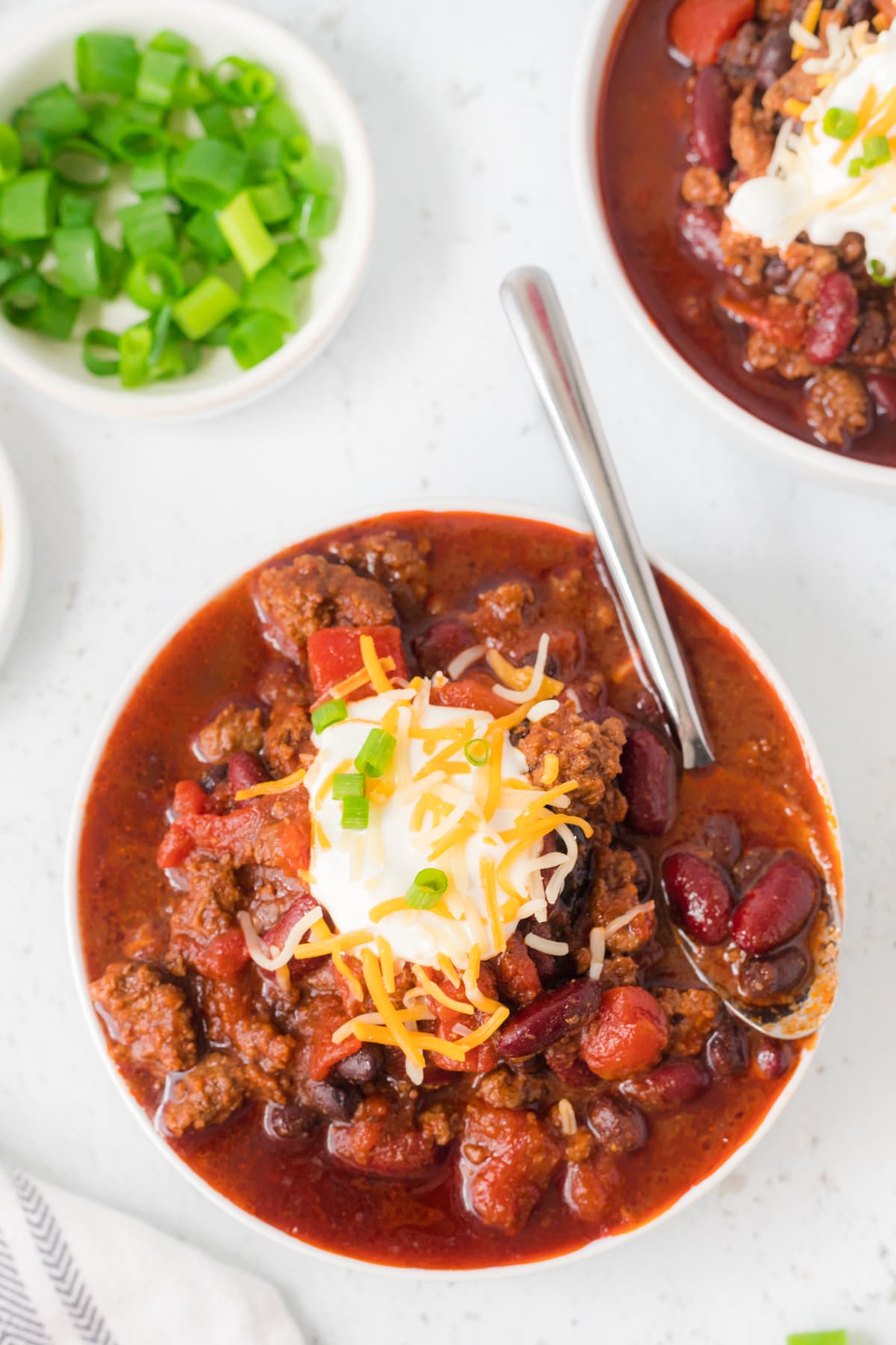 Chili with a spoon in it next to a bowl of chopped green onion.