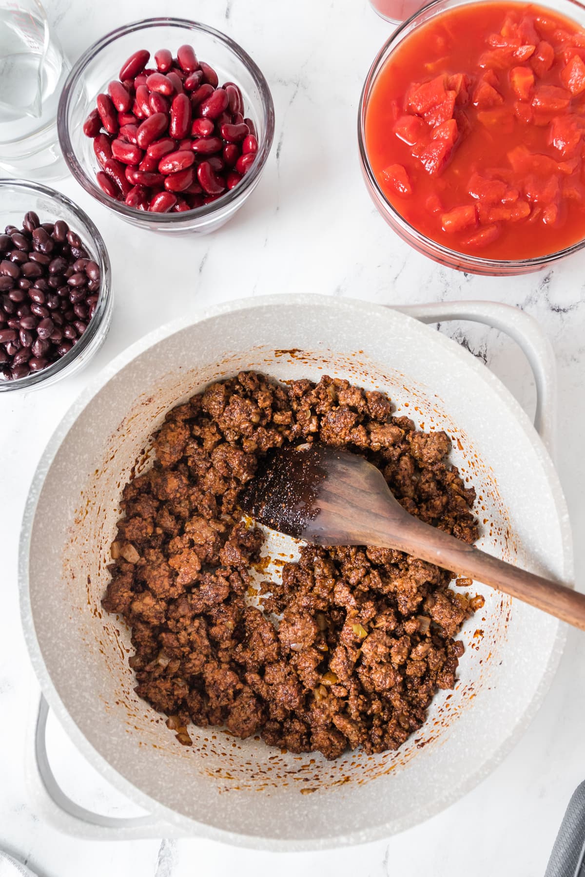Seasoned ground beef in a pan next to diced tomatoes and two kinds of beans.