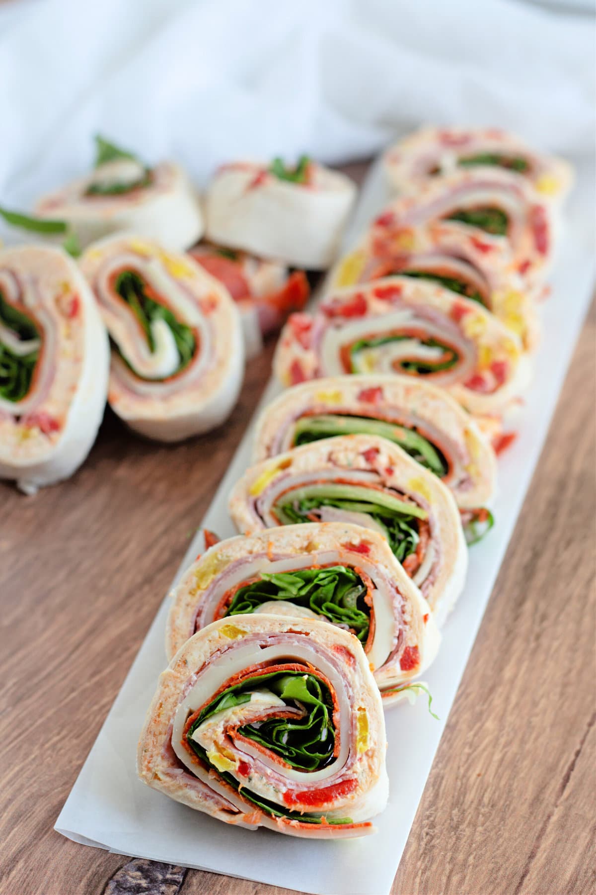 A row of Italian pinwheel sandwiches lined up on a long white platter.