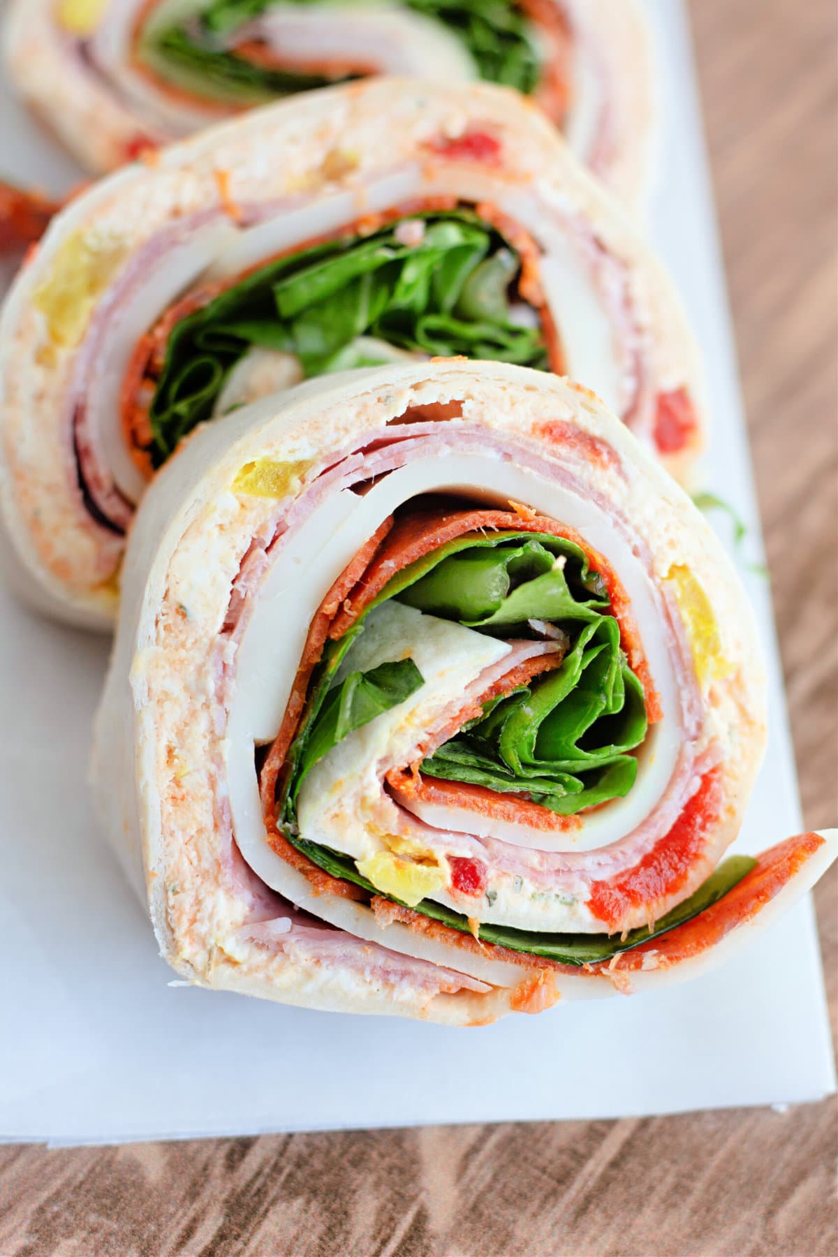 Three Italian pinwheel sandwiches lined up on a white platter.