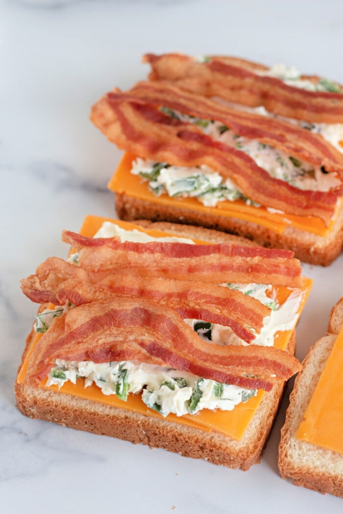 placing bacon onto the grilled cheese sandwiches.