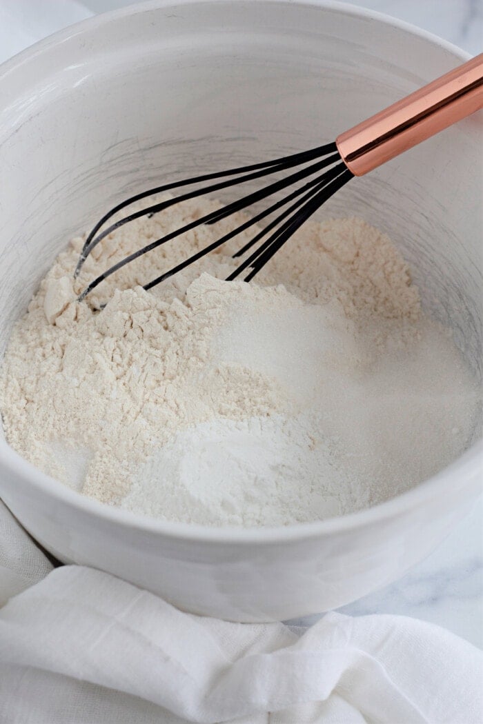 whisking together flour, salt, sugar, and baking powder in a white bowl.
