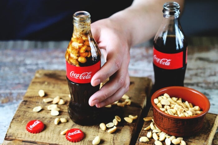 A hand holding a bottle of Peanuts and Coke.