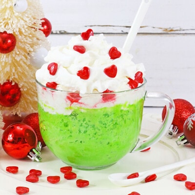 Grinch Mug Cake with whipped cream and hearts on top.