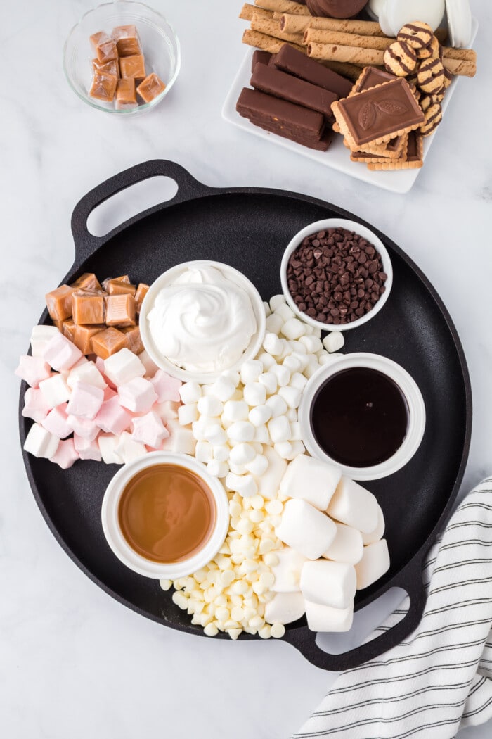 Caramels and chocolate chips added to a hot chocolate charcuterie board with marshmallows and bowls of cocoa mix..