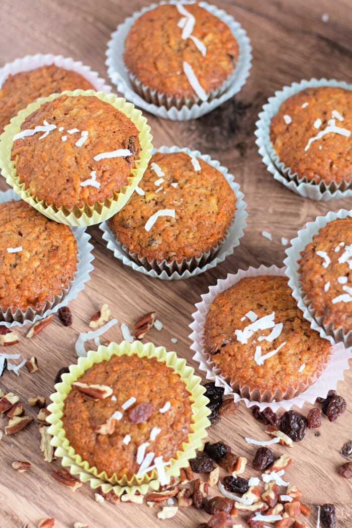 Morning Glory Muffins on a wooden counter with raisins, coconut, and pecans.