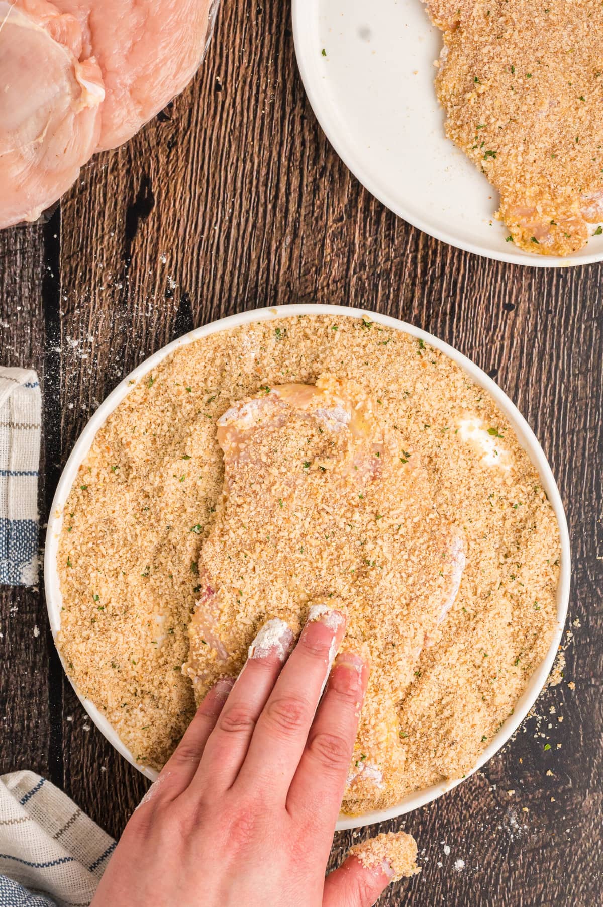 Hands dipping a chicken breast in breadcrumbs