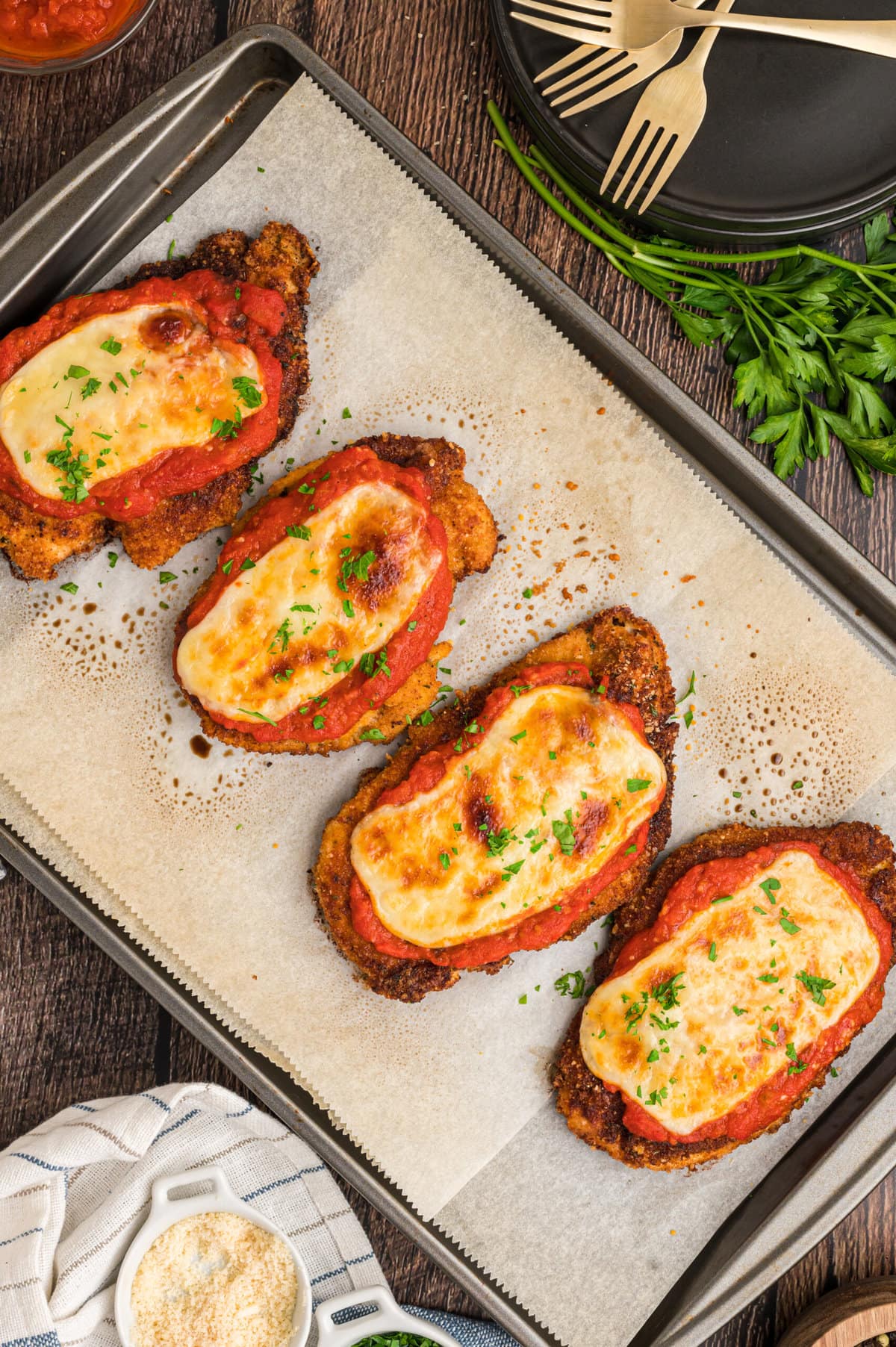 Four pieces of chicken parmesan on a baking sheet